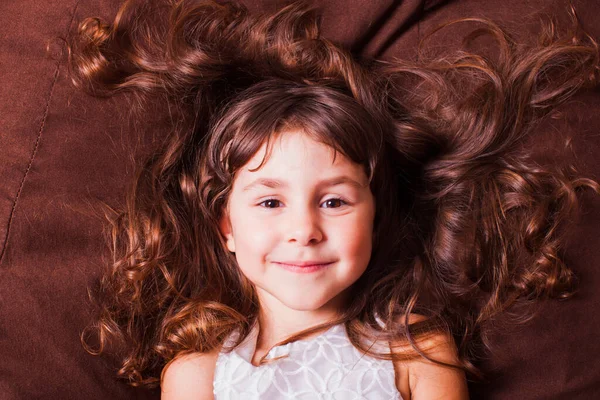 Retrato de rosto de menina bonito com cabelo castanho, deitado no sofá. Sonhos infantis . — Fotografia de Stock