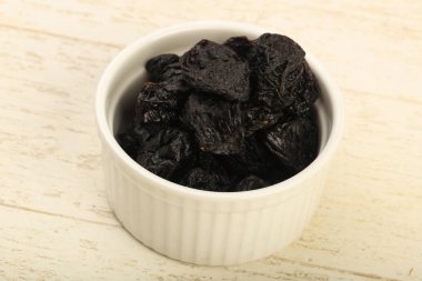 Kurumuş erikler ahşap arka planda kasede yığılıyor.