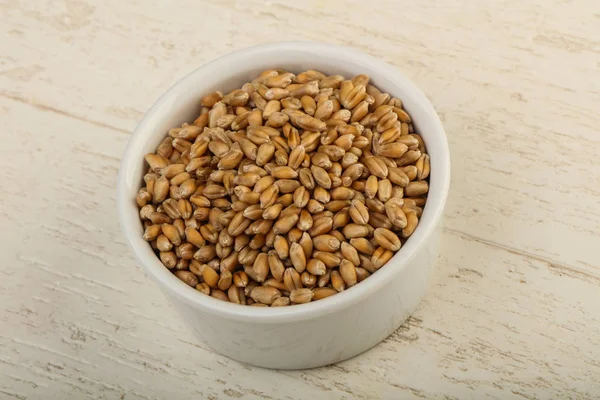 Wheat grains in the bowl over wooden background