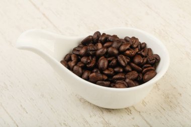 Kavrulmuş kahve çekirdekleri yığın içinde kase ahşap arka plan üzerinde