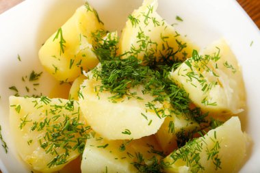 Ahşap arka plan üzerinde beyaz tabakta dereotu ile haşlanmış patates