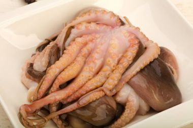 Ahşap arka plan üzerinde yemek pişirmek için hazır beyaz tabakta ham ahtapot