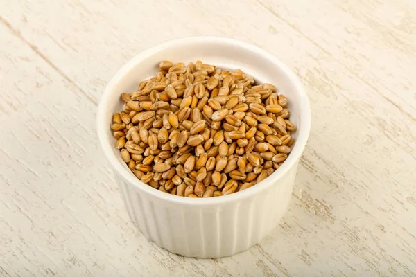 Wheat grains in the bowl over wooden background