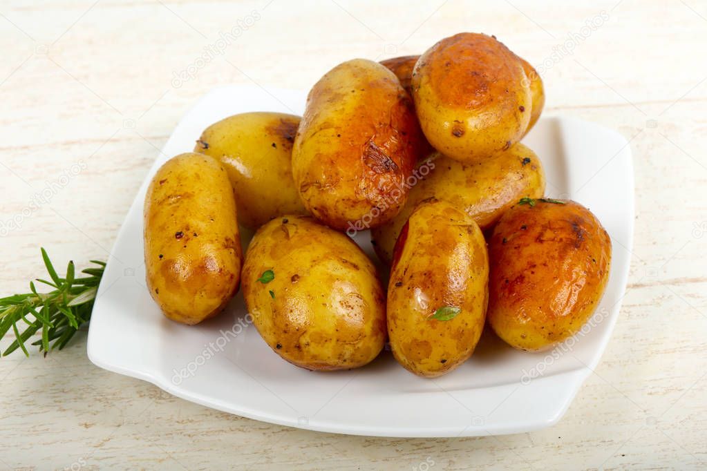 Young baked potato with rosemary over wooden background