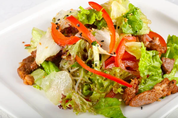 Domuz eti ve beyaz masa üzerinde ızgara sebze salatası