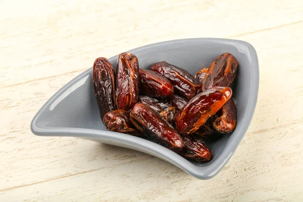 Sweet dates fruits heap in bowl, wooden table background