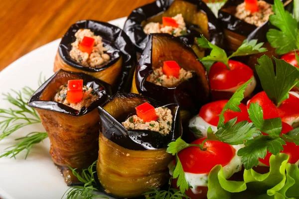 Stuffed eggplant and tomato served salad leaves over wooden background
