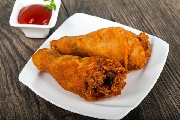 Crispy chicken legs with ketchup over wooden background