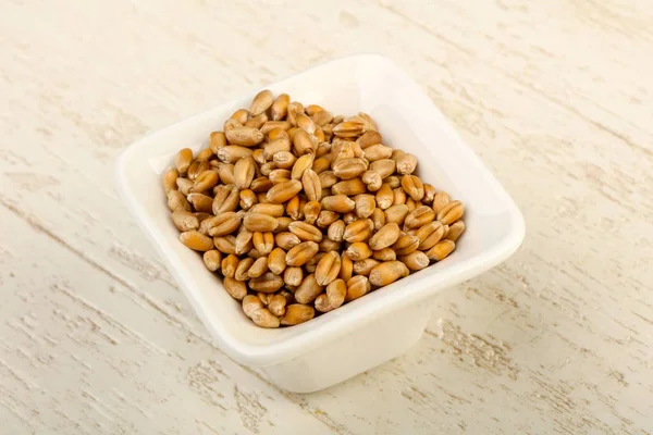 Wheat grains in the bowl over wooden background