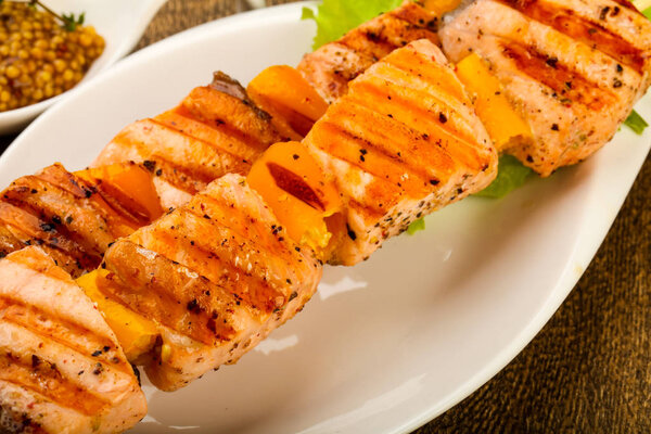Grilled salmon skewer with Dijon mustard sauce on white plate at kitchen wooden table