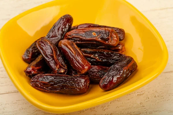 Sweet dates fruits heap in bowl, wooden table background