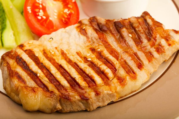 Grilled pork cutlet with sauce and vegetables over wooden background