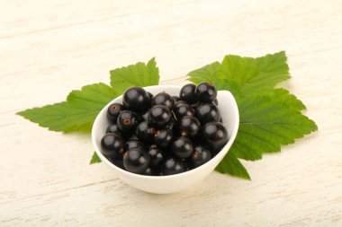 Olgun siyah kuş üzümü yaprağı, ahşap masa arka plan ile kase