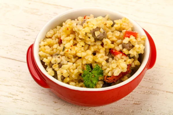 Bulgur tavuk kalpleri ve ahşap arka plan üzerinde kuru domates ile kase