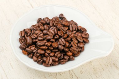 Kavrulmuş kahve çekirdekleri yığın içinde kase ahşap arka plan üzerinde