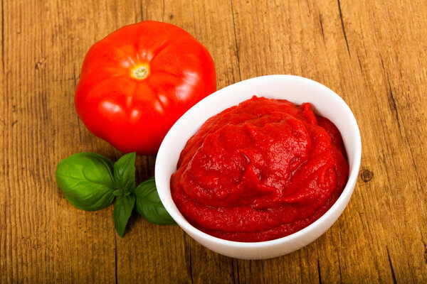 Tomato paste with basil leaves over wooden background