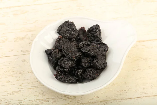 Dried plums heap in bowl over wooden background