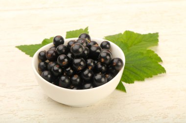 Ahşap arka plan üzerinde yaprak kase olgun siyah kuş üzümü