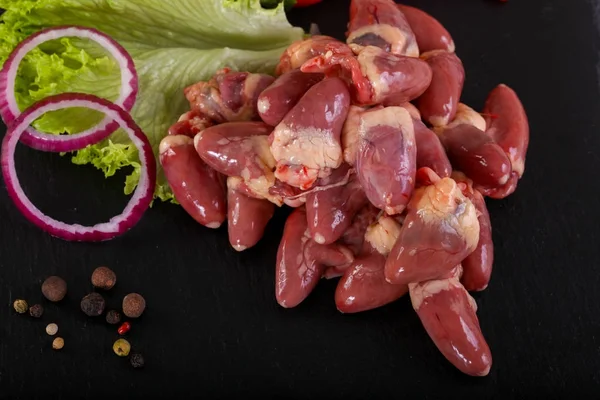 Raw chicken hearts with lettuce over wooden background