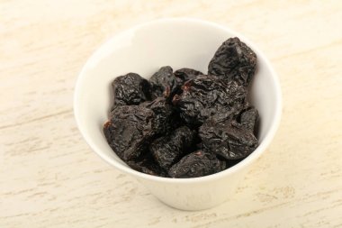 Kurumuş erikler ahşap arka planda kasede yığılıyor.