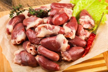 Raw chicken hearts with lettuce over wooden background clipart