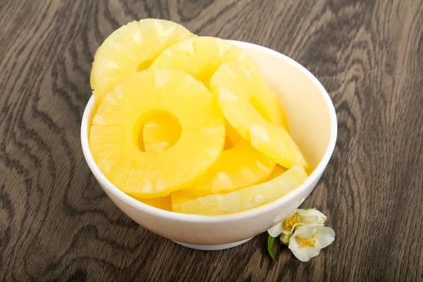Canned pineapple rings in bowl over wooden background
