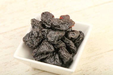 Kurumuş erikler ahşap arka planda kasede yığılıyor.