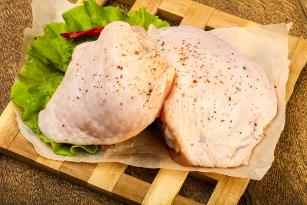 Raw chicken thigh with spices ready for cooking over wooden background