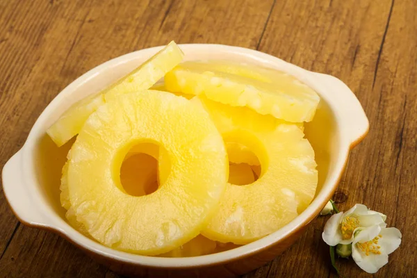 Canned pineapple rings in the bowl over wooden background