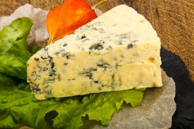 Ahşap arka planda salata yapraklı mavi peynir.