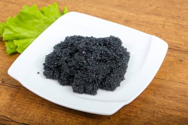 Siyah havyar kase ahşap arka plan üzerinde beyaz plaka