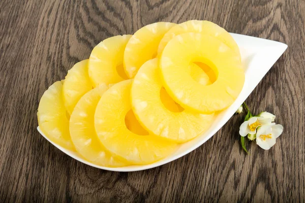 Canned pineapple rings in the bowl over wooden background