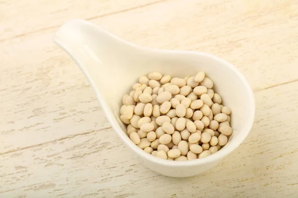 Dry white beans in the bowl over wooden background