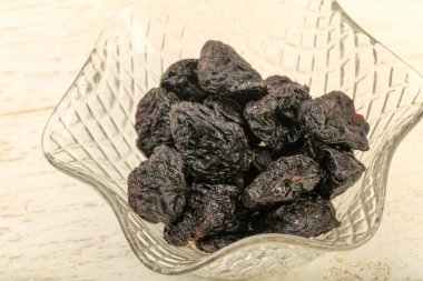 Kurumuş erikler ahşap arka planda kasede yığılıyor.