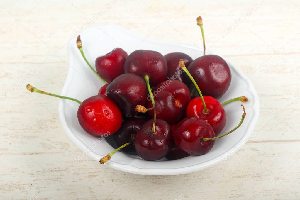 Sweet cherries in the bowl over wooden background