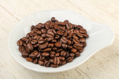 Kavrulmuş kahve çekirdekleri yığın içinde kase ahşap arka plan üzerinde