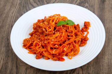 Bolognese makarna ahşap arka plan üzerinde beyaz tabakta fesleğen ile
