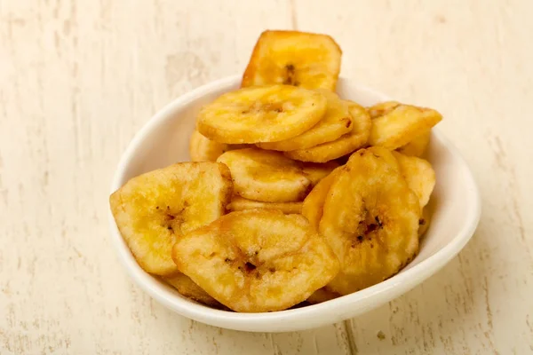 Dry banana chips on white plate over wooden background