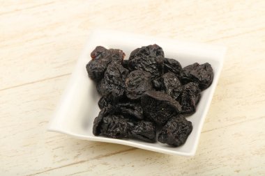 Kurumuş erikler ahşap arka planda kasede yığılıyor.