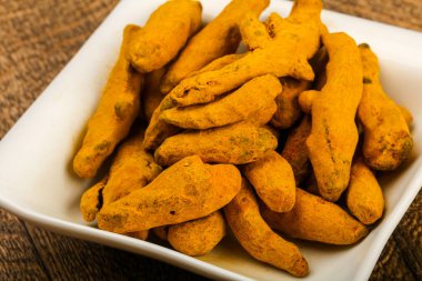 Tumeric kökü yığın içinde kase ahşap arka plan üzerinde