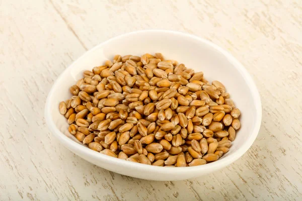 Wheat grains in the bowl over wooden background