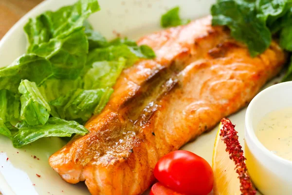 Grilled salmon steak with sauce and salad leaves