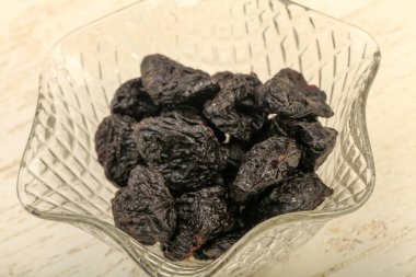 Kurumuş erikler ahşap arka planda kasede yığılıyor.