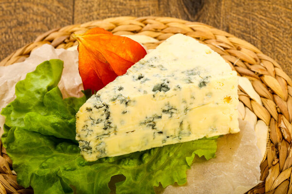 Blue cheese with salad leaves over the wooden background