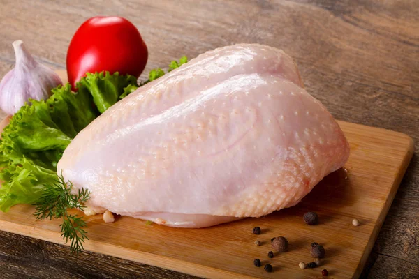 Raw chicken breast with skin over wooden background