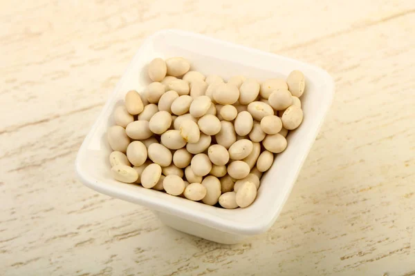 Dry white beans in the bowl over wooden background