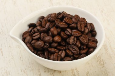 Kavrulmuş kahve çekirdekleri yığın içinde kase ahşap arka plan üzerinde