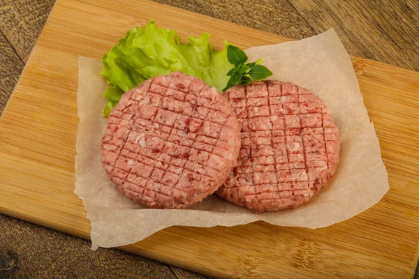 Raw burger cutlets with salad leaves ready for grill over wooden background