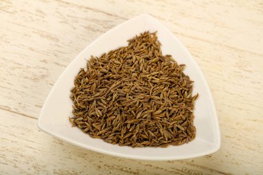 Cumin seeds heap in the bowl over wooden background clipart