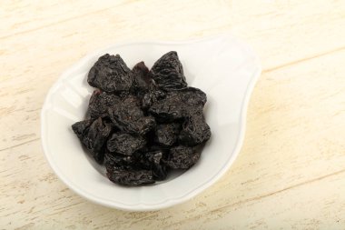 Kurumuş erikler ahşap arka planda kasede yığılıyor.